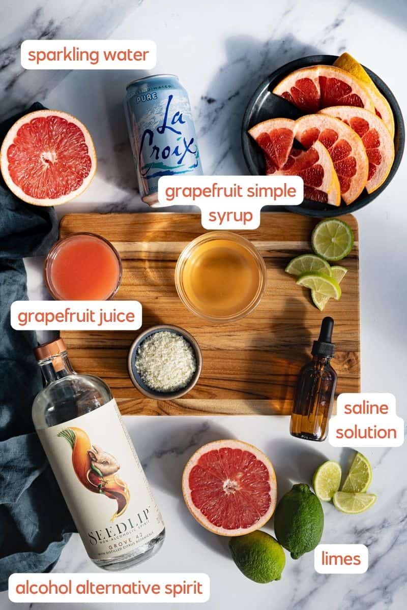 A labeled ingredient shot for a paloma mocktail. Ingredients used to make the mocktail sit on a cutting board and countertop.