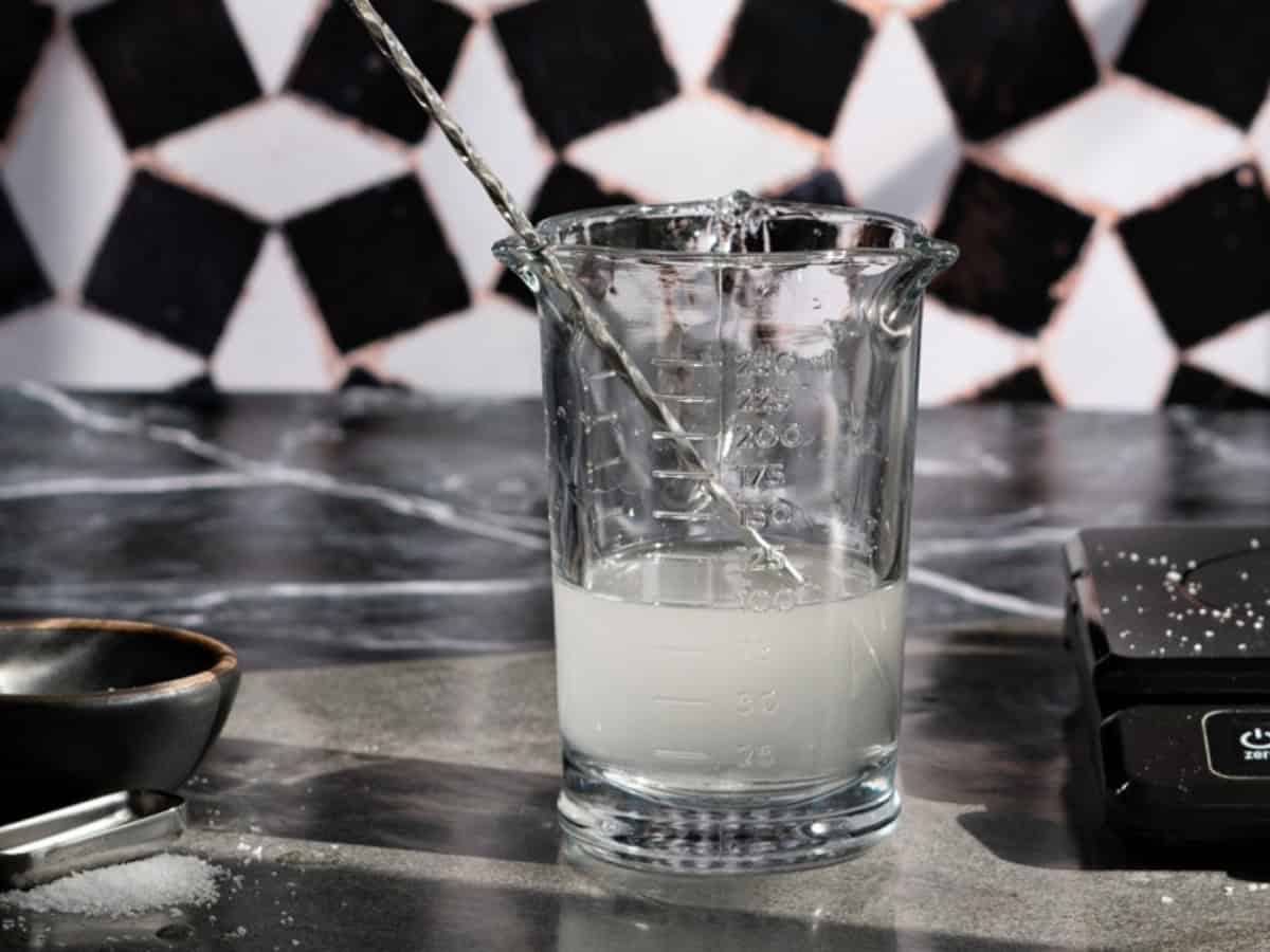 Showing the process of kosher salt dissolving in a glass of water to make a saline solution. The water is cloudy because of the salt which has not fully dissolved.