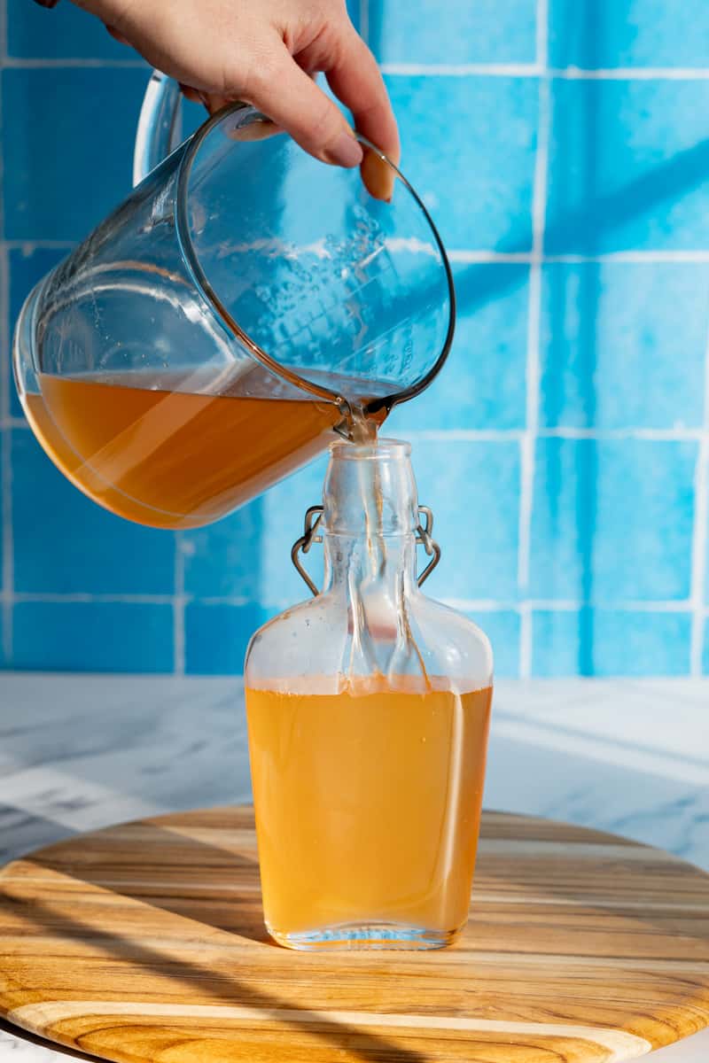 Pouring grapefruit simple syrup that has been strained into a glass bottle with a stopper for storage.