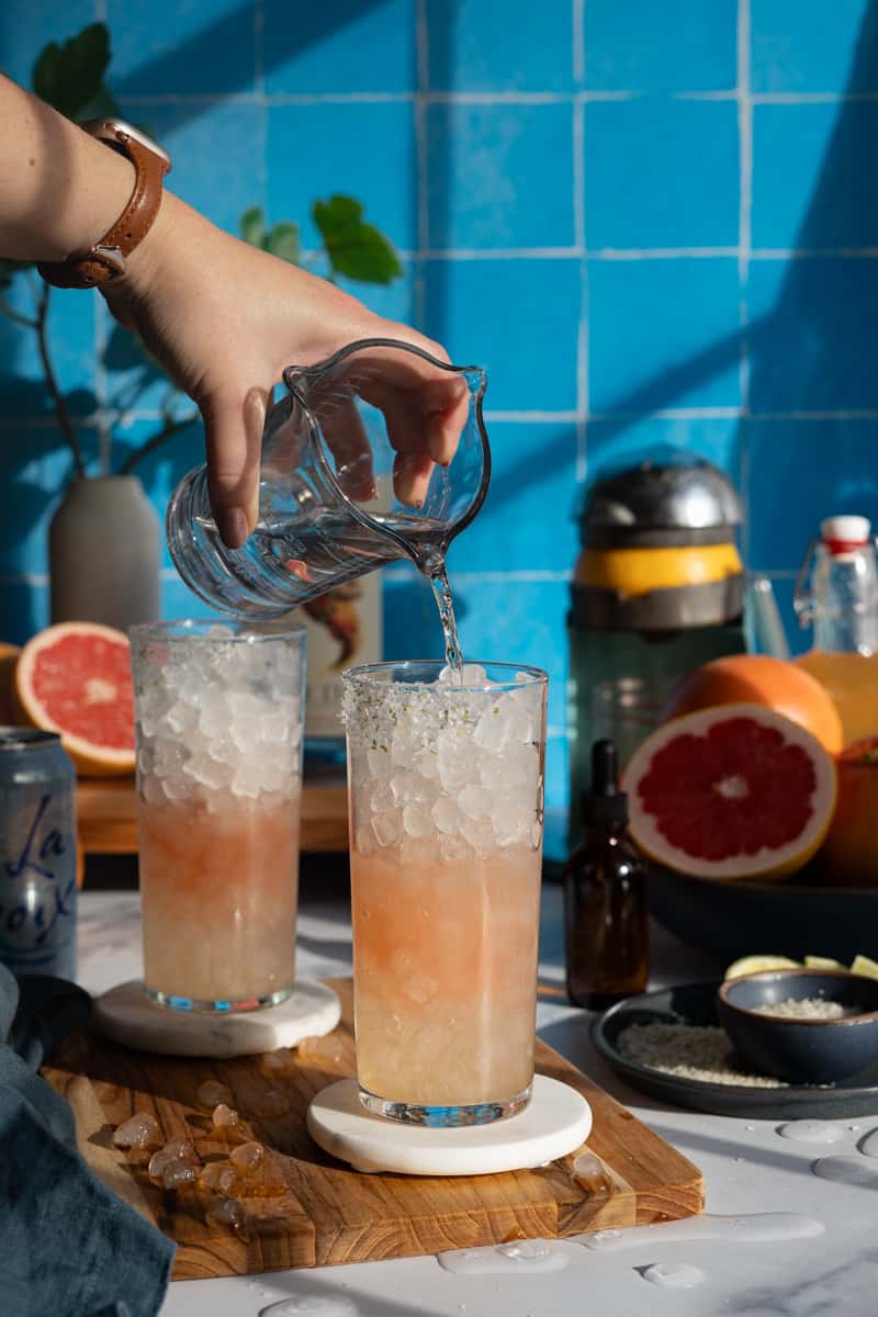 Pouring in an alcohol alternative spirit into a paloma mocktail.