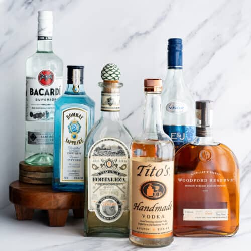 A collection of liquor bottles sit on a marble countertop to showcase the six main types of liquor.