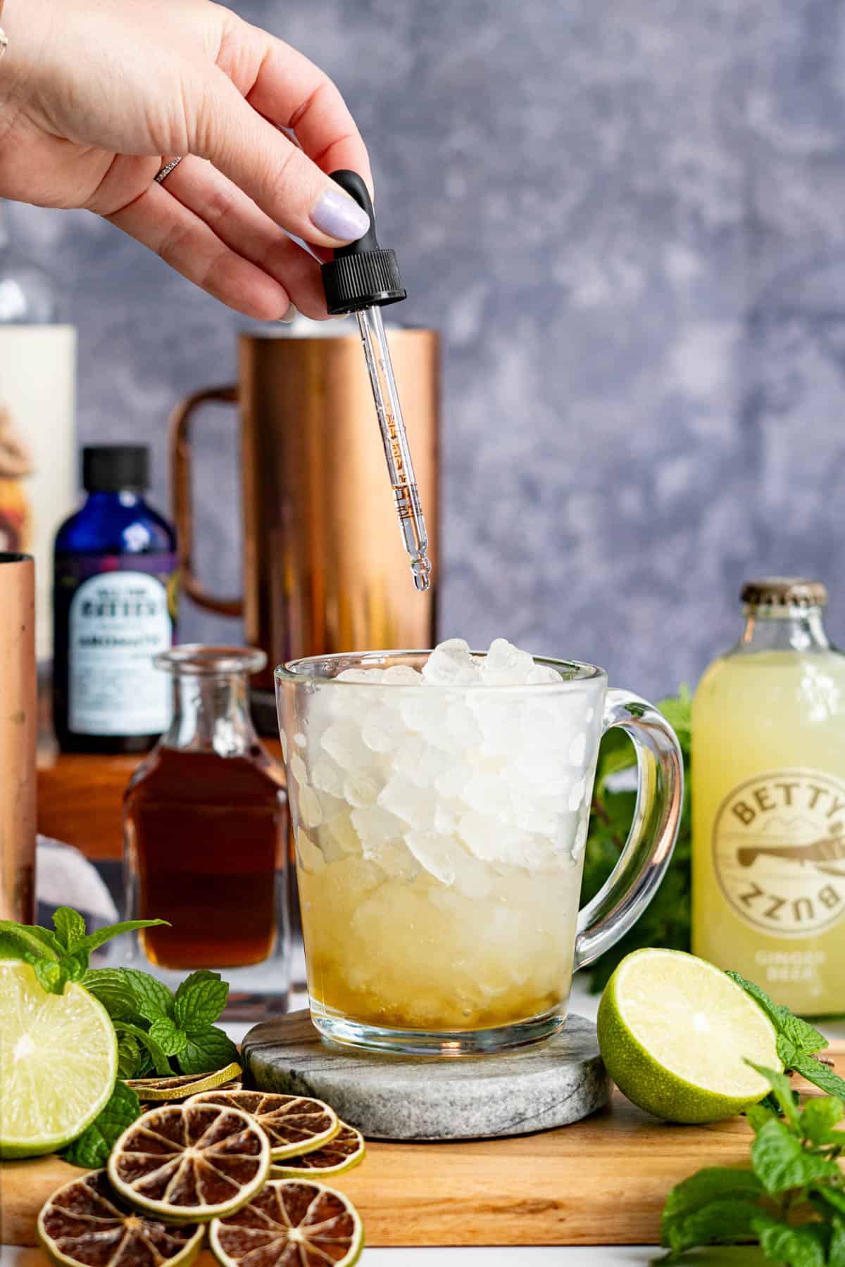 A hand from out of frame is dropping a saline solution into a virgin moscow mule cocktail.