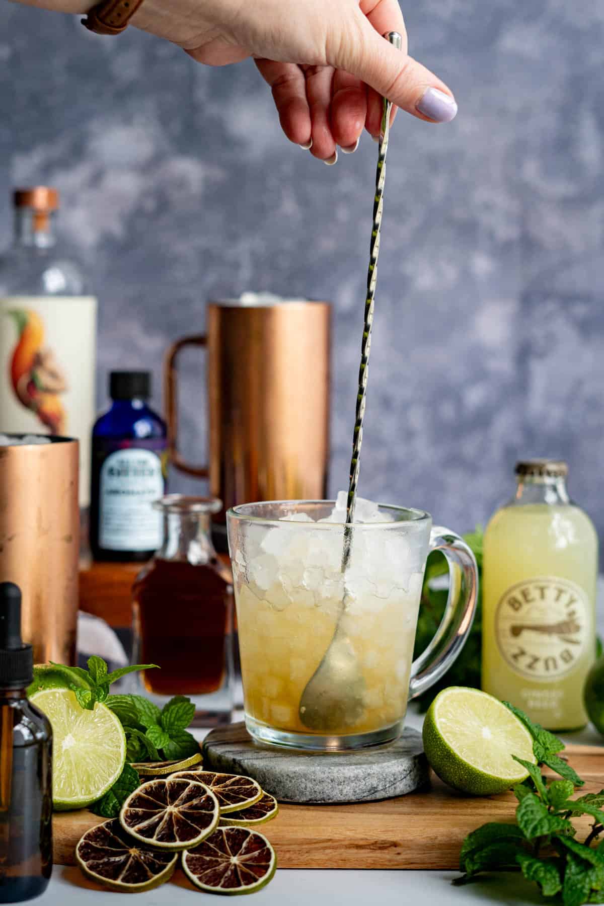 A hand from out of frame is stirring a virgin moscow mule with a cocktail stirring spoon.