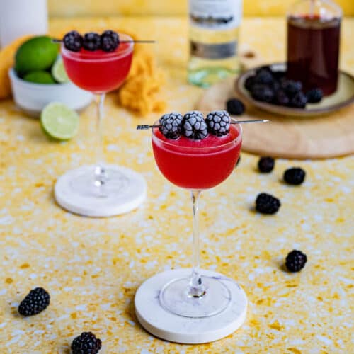 Two blackberry daiquiri cocktails sit on a yellow terrazzo countertop on coasters ready to be served.