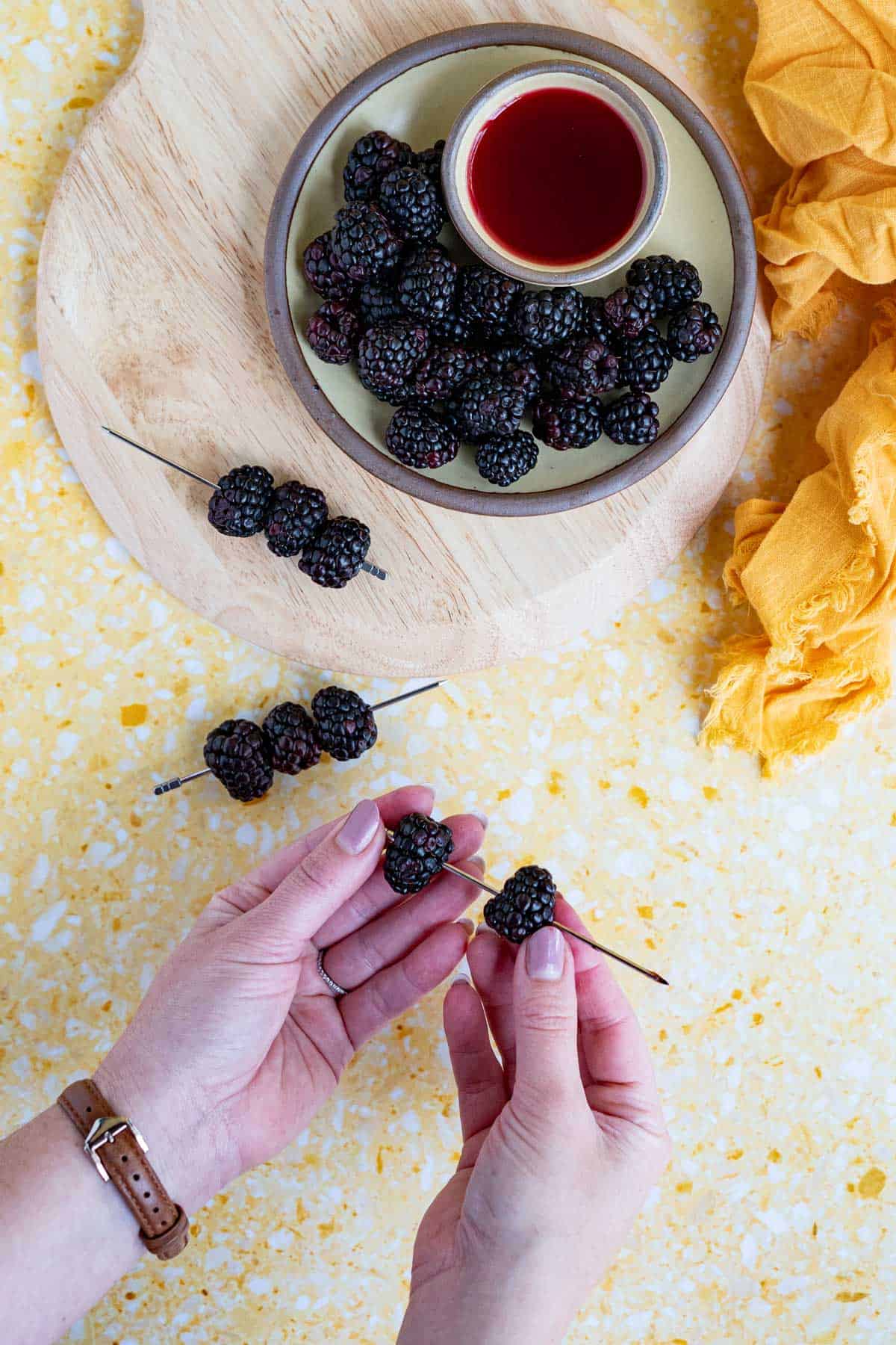 Two hands from out of frame are skewering blackberries onto a cocktail pick to be used as a garnish for a blackberry daiquiri.