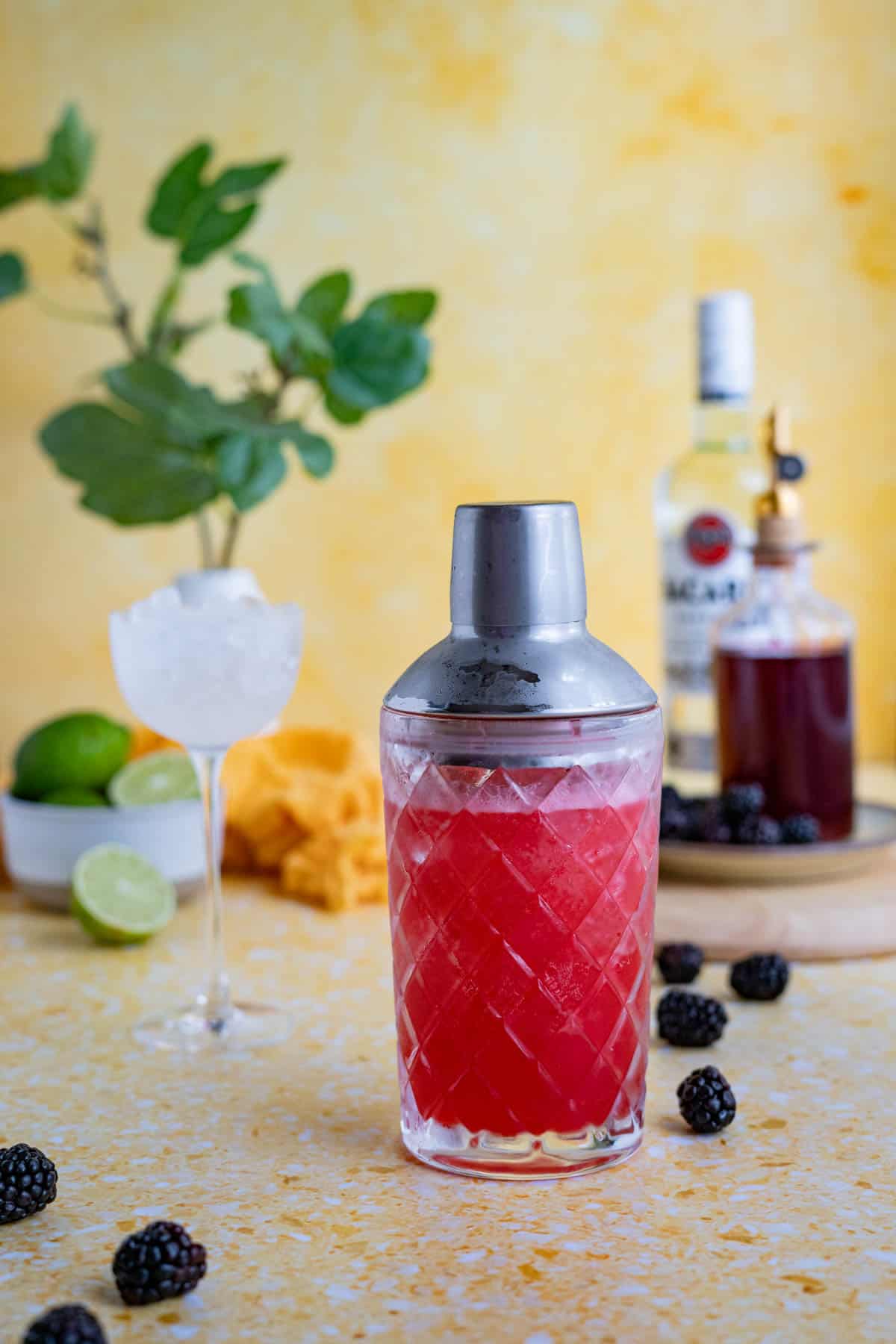 A cocktail shaker filled with a blackberry daiquiri recipe sits on a yellow countertop.