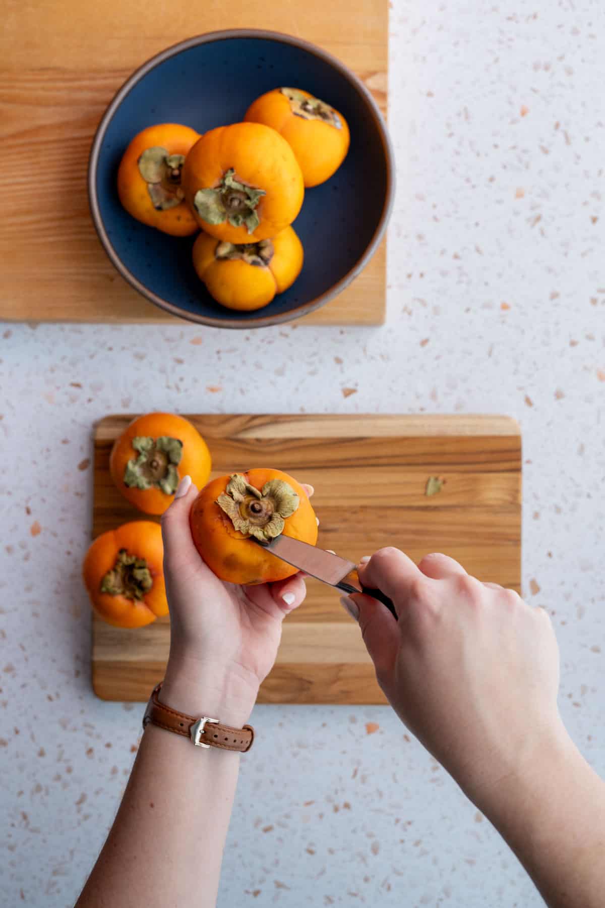 A hand from out of frame is cutting the tops of persimmons to remove the core and leaves.