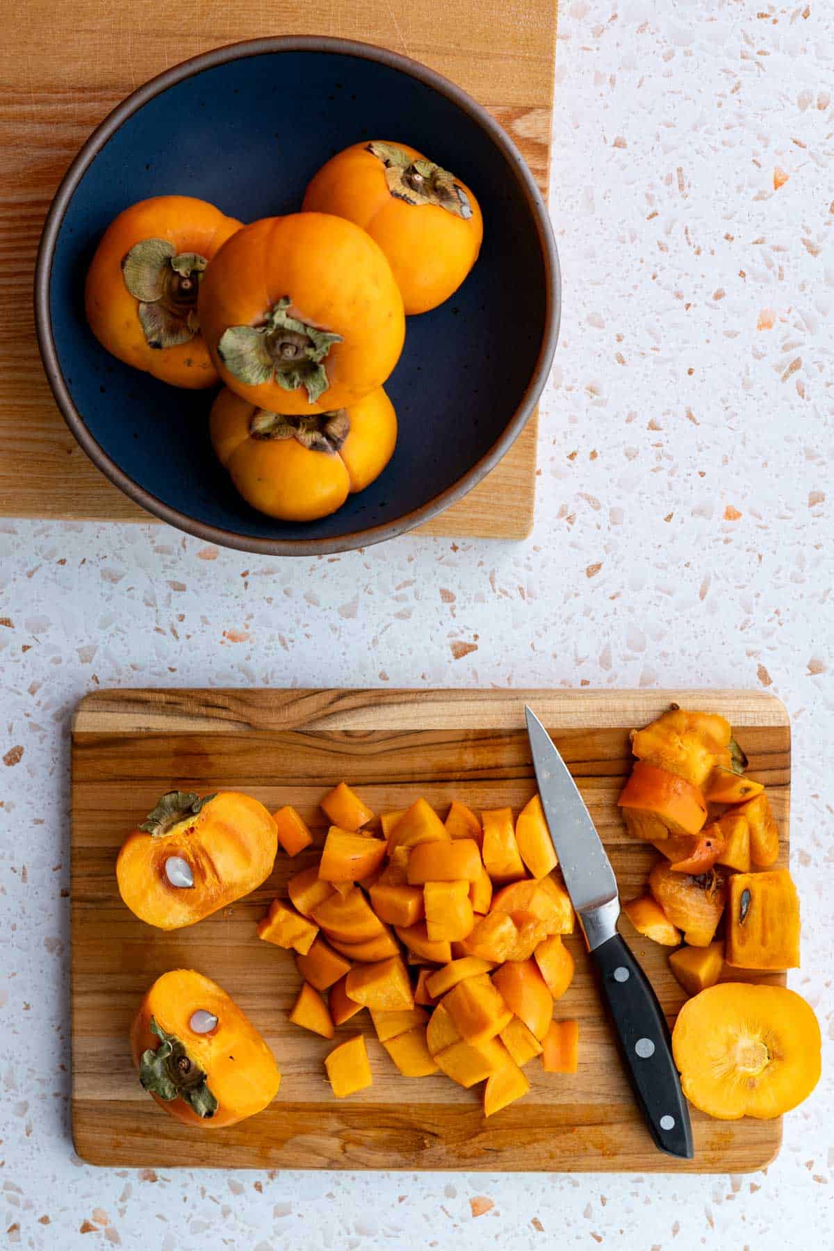 Chopped persimmons are sitting on a cutting board next to a pairing knife.
