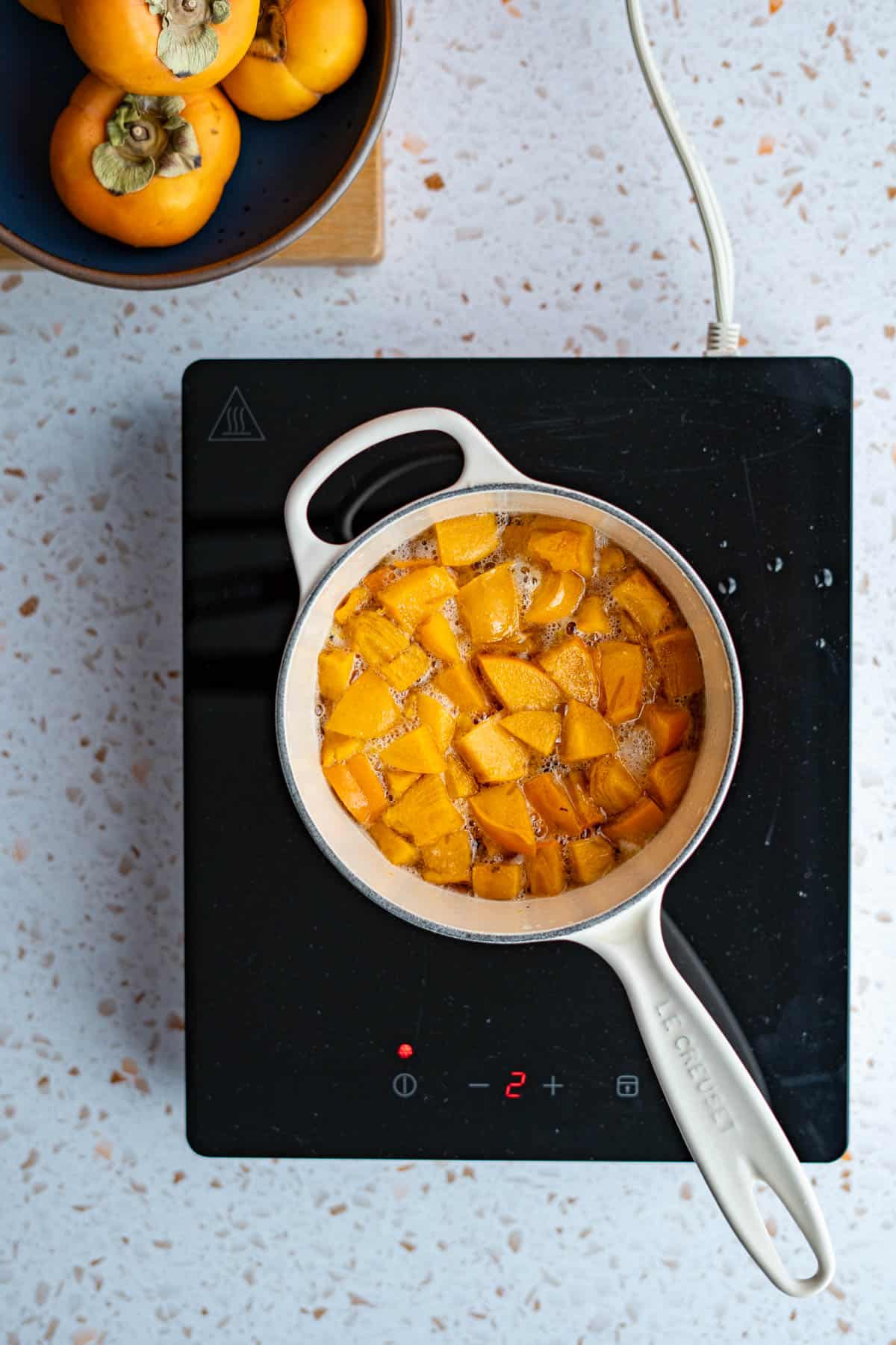 Persimmon simple syrup is simmering in a saucepan on a hotplate.