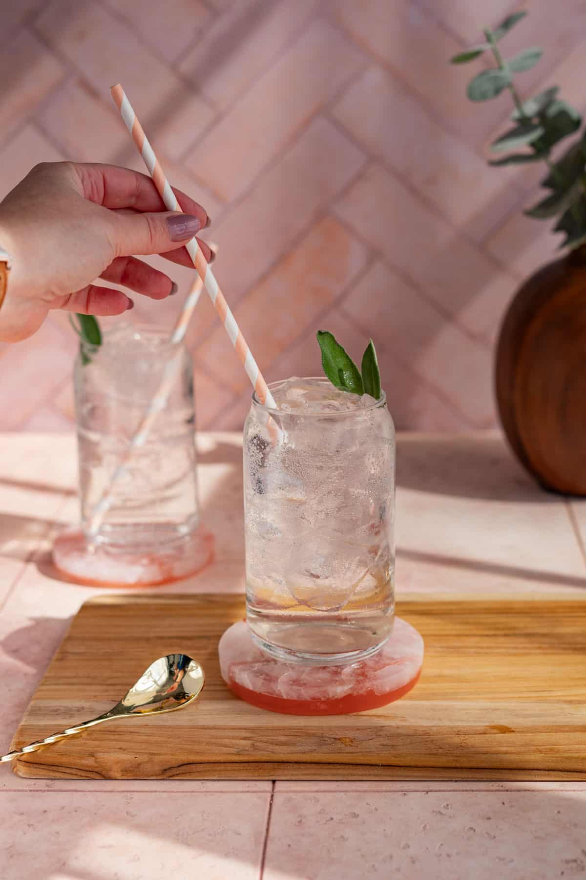 A hand from out of frame is adding a striped paper straw to a homemade sage soda.