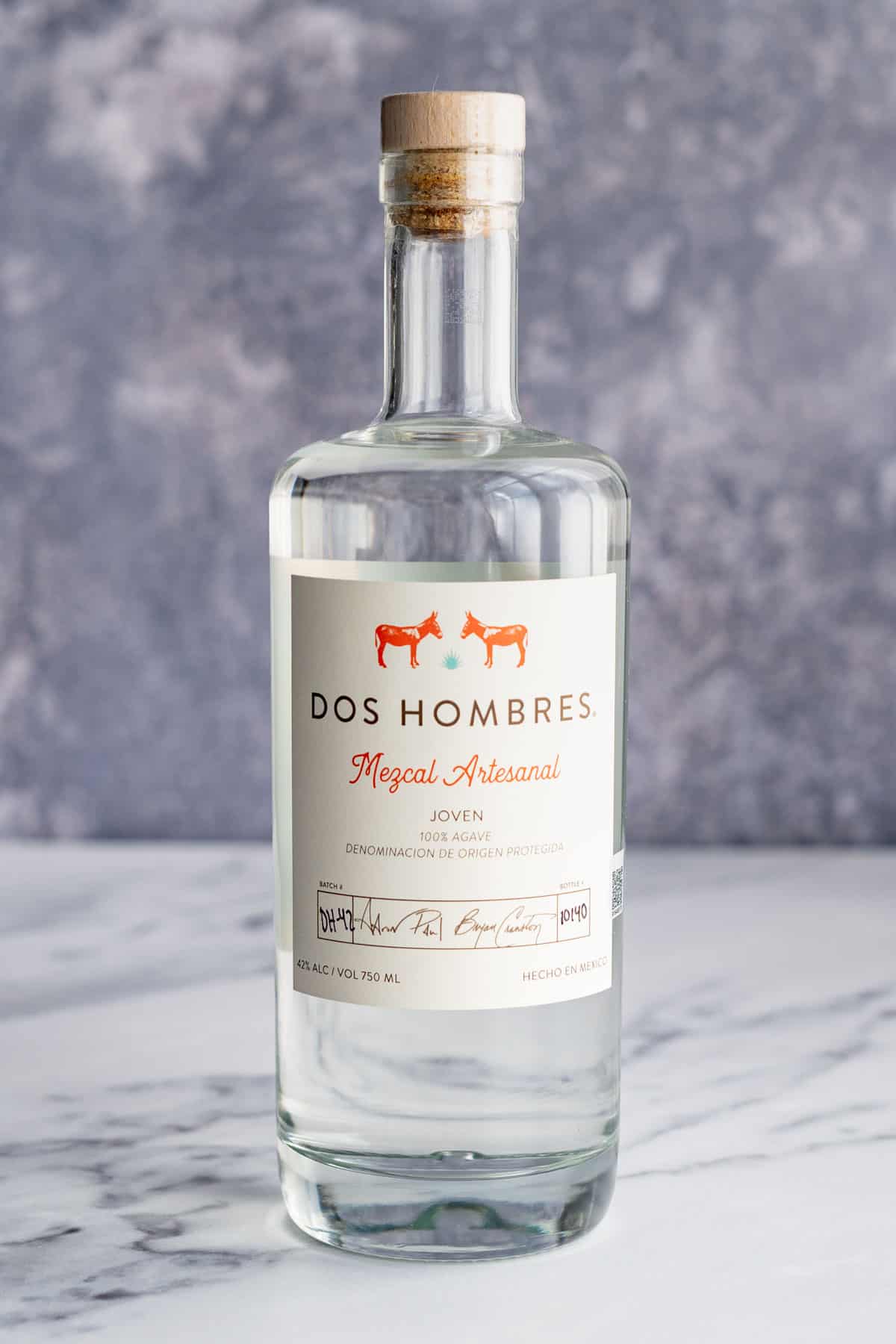 A bottle of mezcal sits on a white marble countertop.