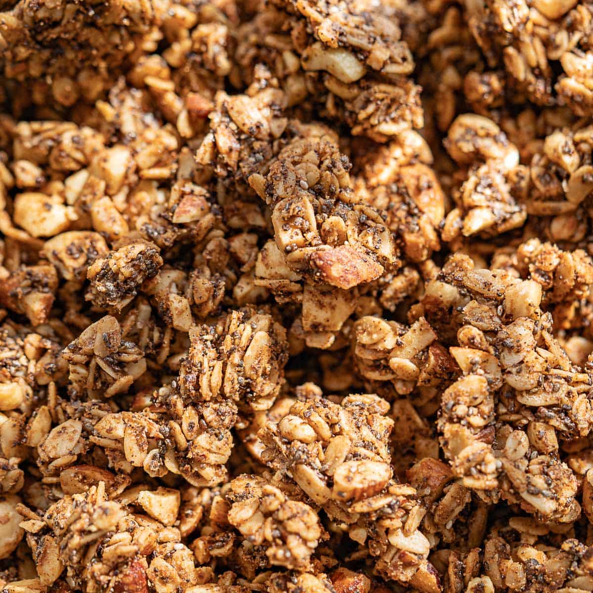 Close-up of clusters of coffee granola containing oats, nuts, and seeds, showing a crunchy texture and golden-brown color.
