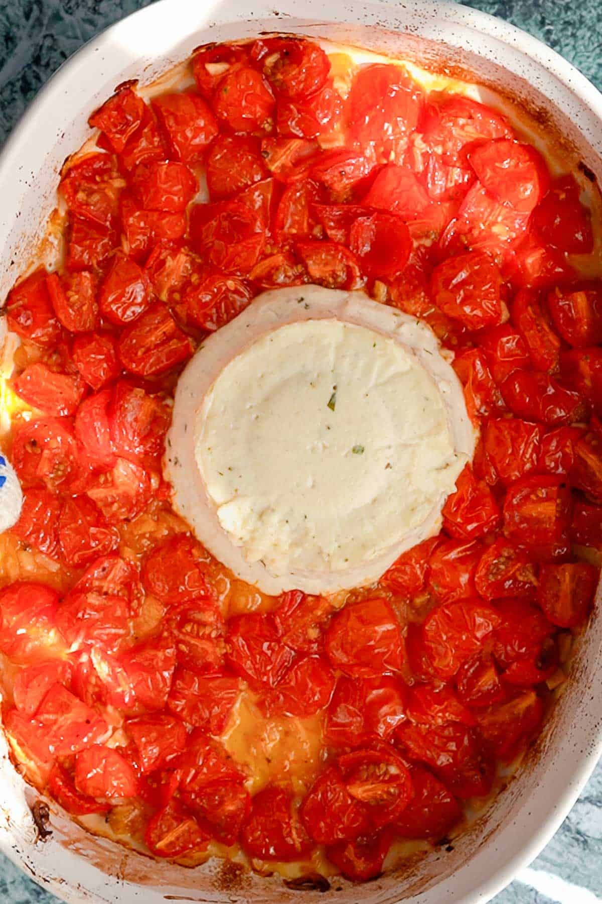 A baked Boursin cheese block surrounded by roasted cherry tomatoes in a white dish, viewed from above.