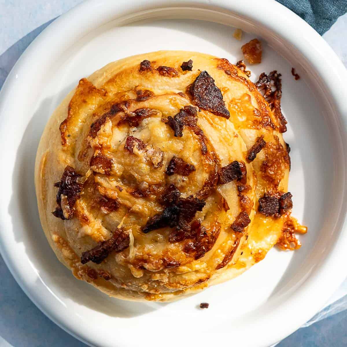 A close-up of delicious bacon and cheese rolls, topped with melted cheese and crispy bacon bits, served on a white plate.