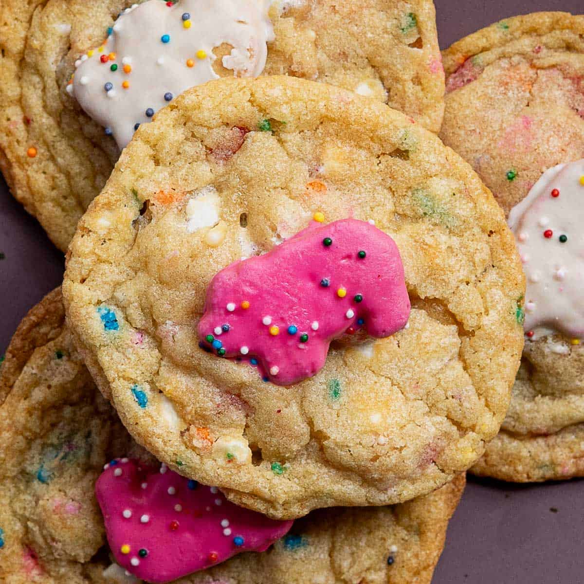 Close-up of cookies topped with circus animal cookies, featuring pink and white frosted animal crackers and colorful sprinkles, stacked on top of each other.