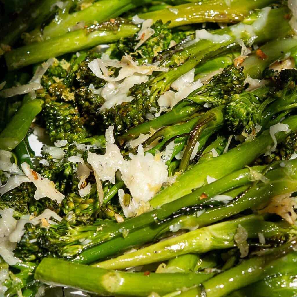 Close-up of roasted broccolini, perfectly topped with melted grated cheese and seasoned with herbs, glistening with olive oil.